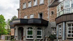 A multi-story building with a stone facade, a black awning with the word "VINTAGE" on it, and a set of stairs leading to the entrance. - Hotel Vintage (Pulheim)