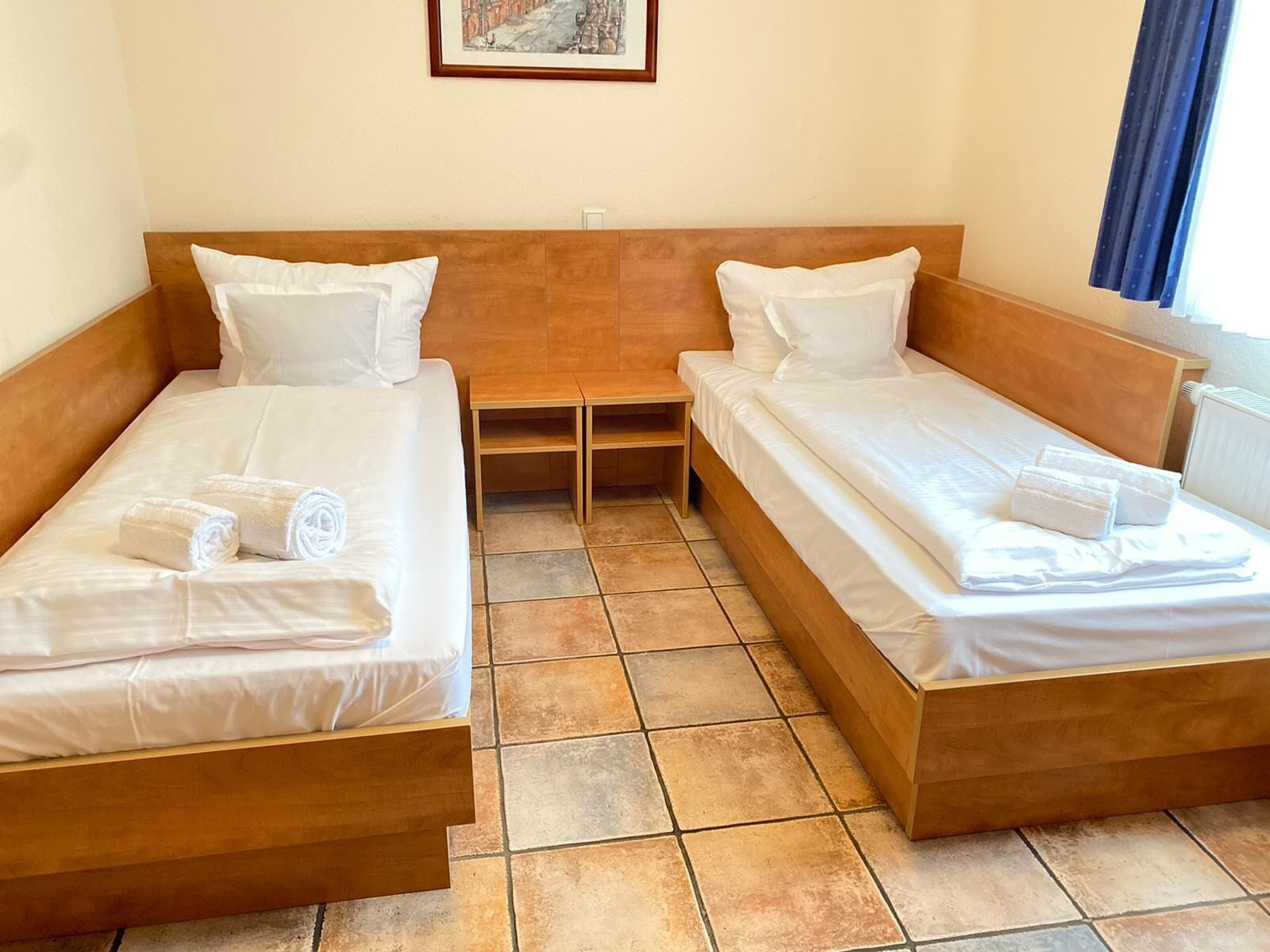 A twin room with two single beds, a small wooden table, and a framed picture on the wall.