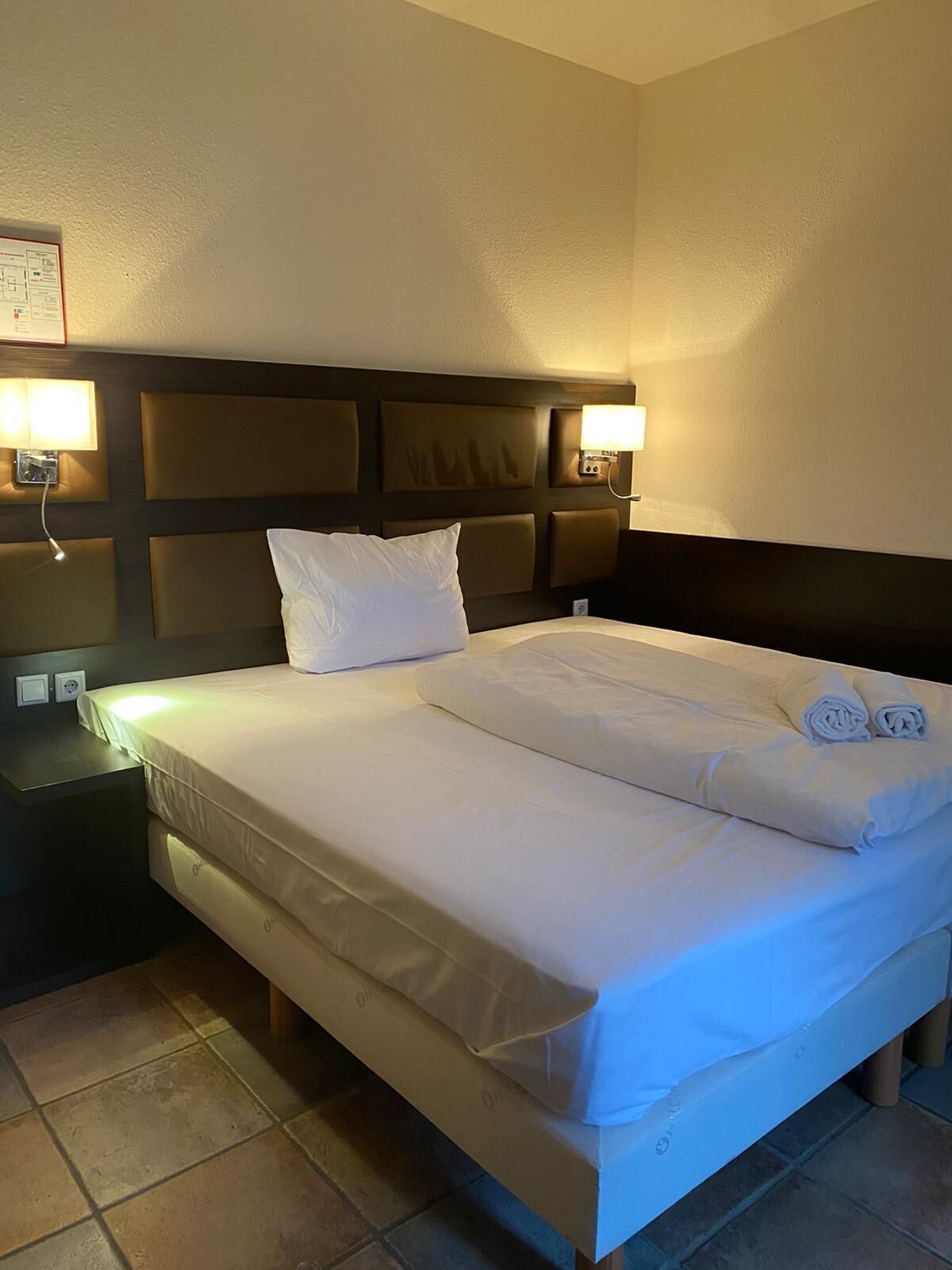A hotel room with a large bed, two bedside tables, and wall-mounted lamps.