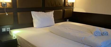A hotel room with a large bed, two bedside tables, and wall-mounted lamps.