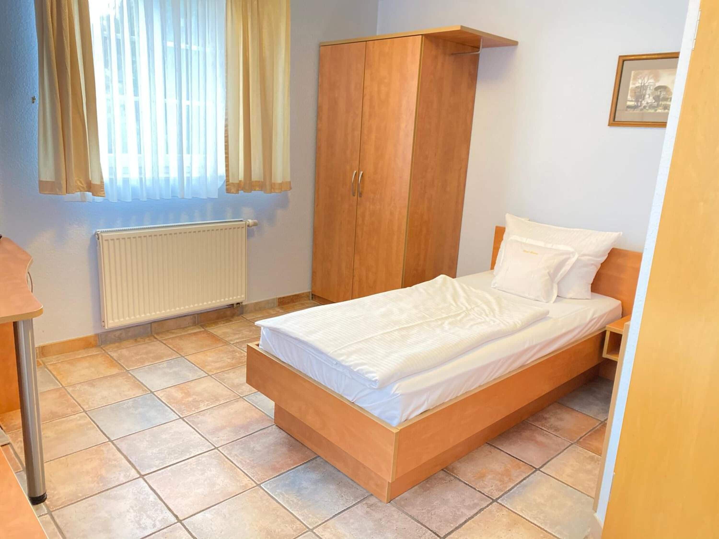 A bedroom with a wooden bed, a wardrobe, a radiator, and a window with curtains.