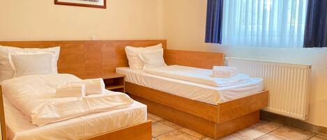 A hotel room with two single beds, a nightstand, a framed picture on the wall, and a window with curtains.
