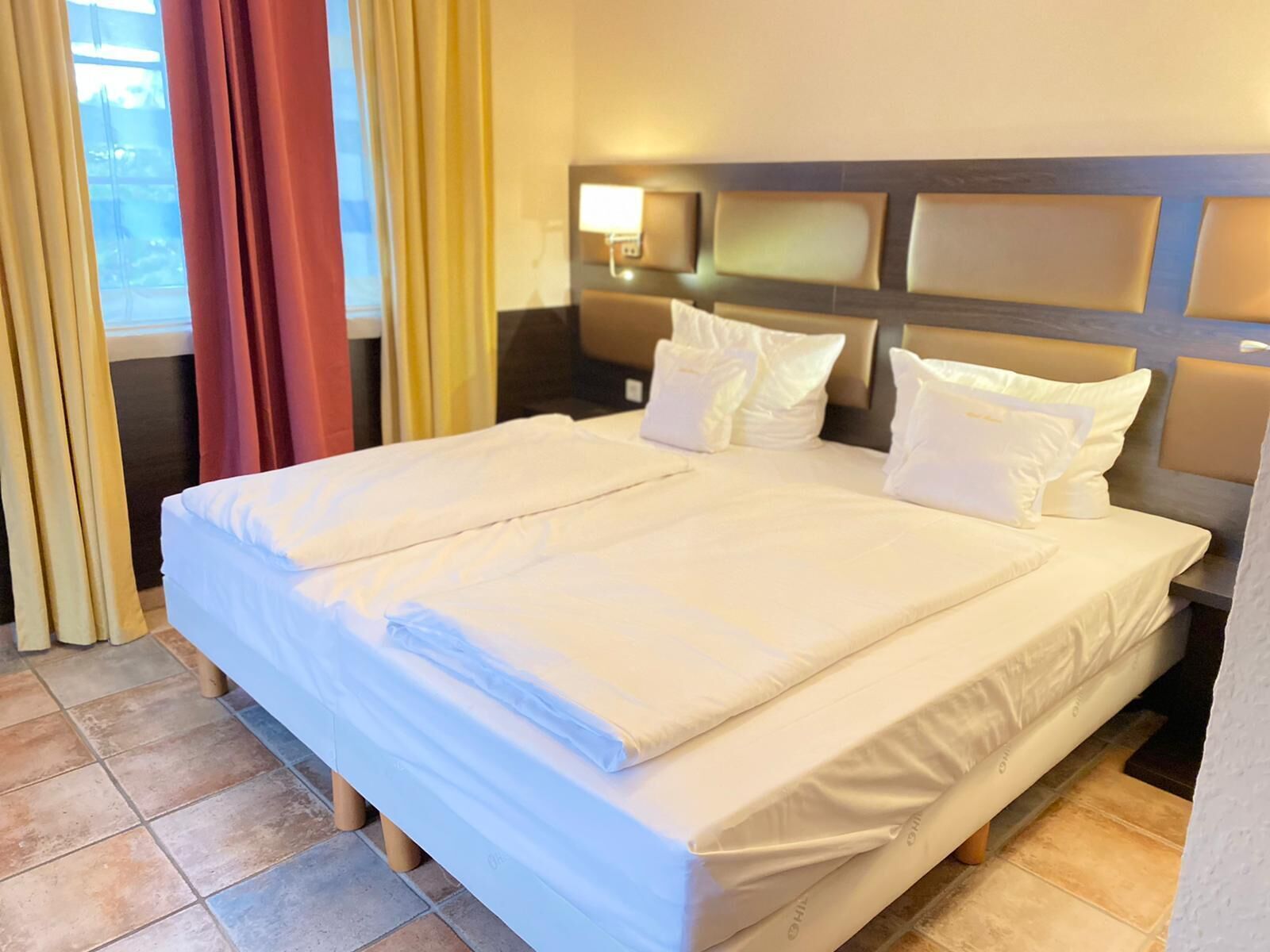 Een hotelkamer met een groot bed, een nachtkastje en een raam met gordijnen.