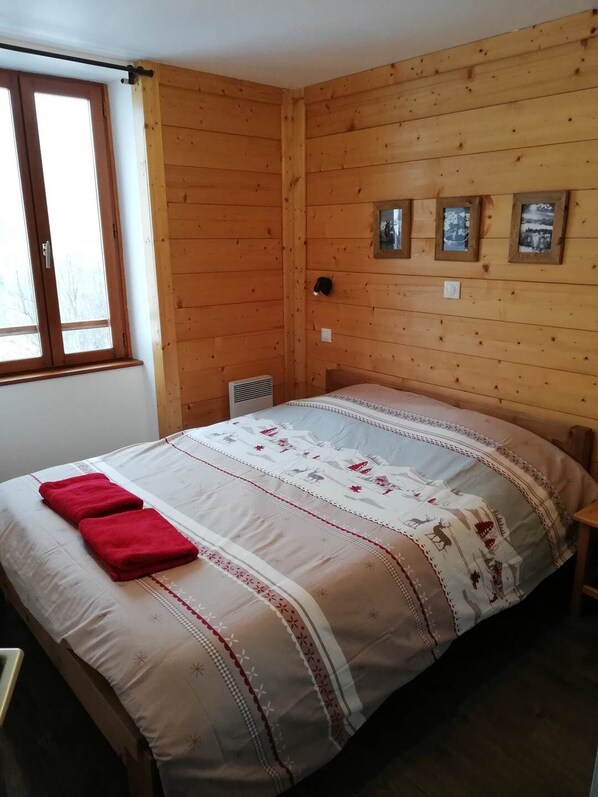A wooden-paneled room with a bed, a window, and three framed pictures on the wall.