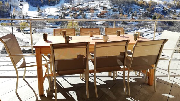 A dining area with a table and chairs, overlooking a snowy mountain village. - Gîte 1- 8 persons- 4 bedrooms- Covered terrace (VALMEINIER)