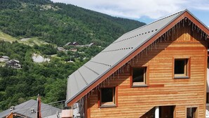 A wooden cabin with a sloped roof, a stone foundation, and a balcony with chairs. - Gîte 1- 8 persons- 4 bedrooms- Covered terrace (VALMEINIER)