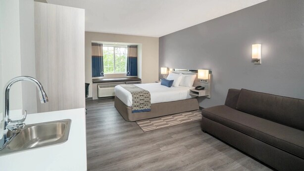 Een hotelkamer met een bed, een slaapbank, een raam met gordijnen, een wandlamp en een wastafel.