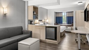 Een compacte hotelkamer met een kitchenette, een bank, een eettafeltje en een bed.