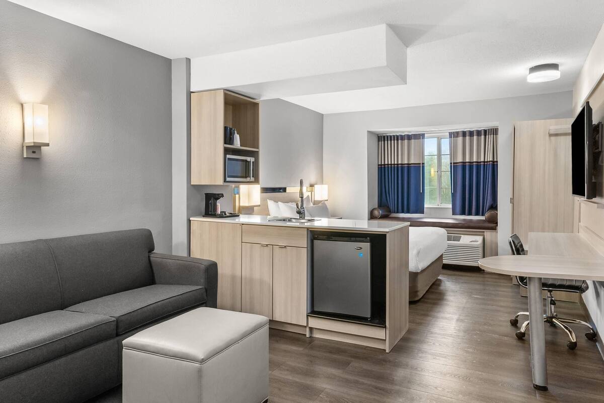 Habitación de hotel compacta con kitchenette, sofá, una mesita y cama.