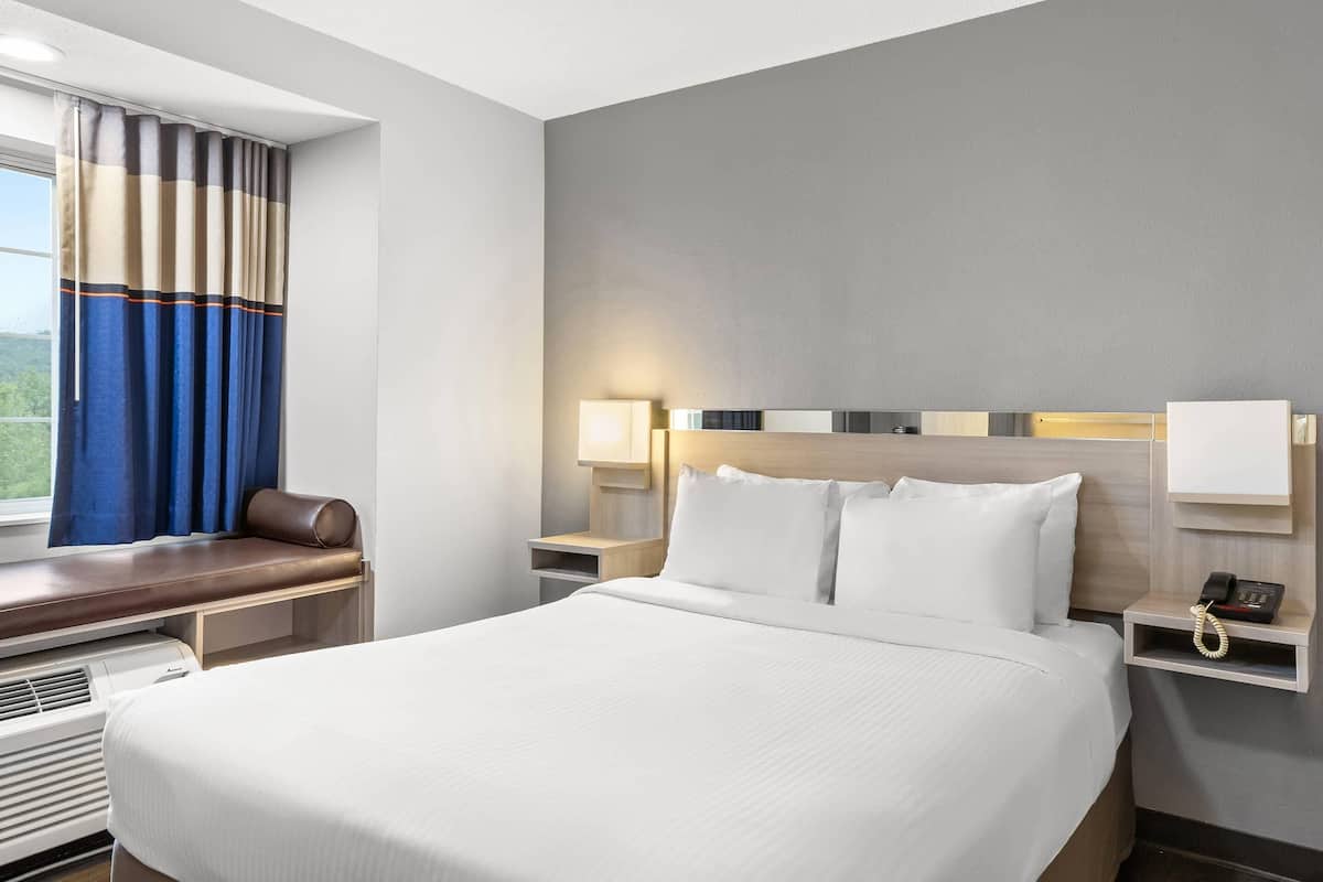 Una habitación de hotel con una cama grande, una mesita de noche con lámpara, teléfono y una ventana con cortinas.