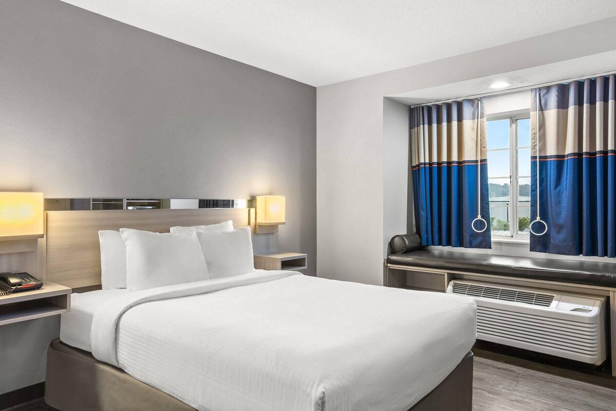 Habitación de hotel con una cama grande, lámparas de noche, una ventana con cortinas y vistas al exterior.