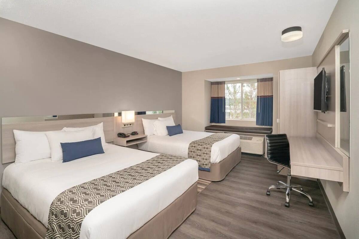 Habitación de hotel con dos camas, un escritorio, una silla, un televisor y una ventana con cortinas.