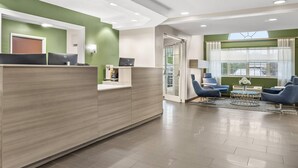 Een receptiegedeelte met een houten receptiebalie, een computer en een zithoek met blauwe stoelen en een bijzettafeltje.