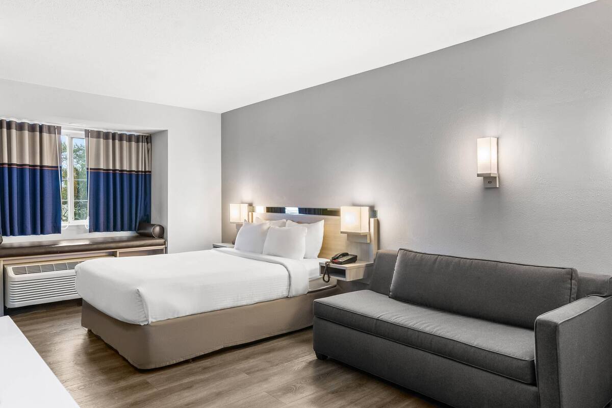 Habitación de hotel con cama, sofá, mesita de noche con lámpara y aplique de pared.