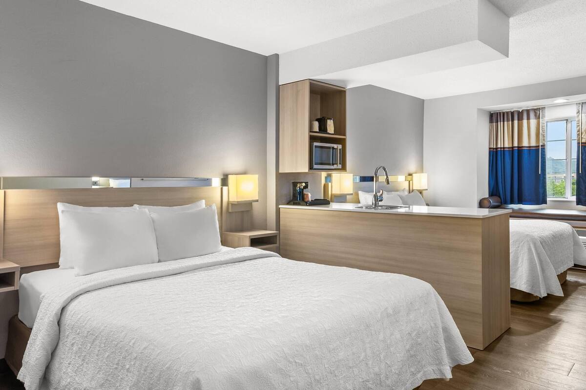 Habitación de hotel con dos camas, un escritorio de madera, microondas y una ventana con cortinas.