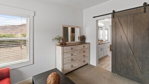Une pièce avec une commode en bois, un miroir, une porte coulissante de style rustique et une vue sur une cuisine par une porte ouverte.