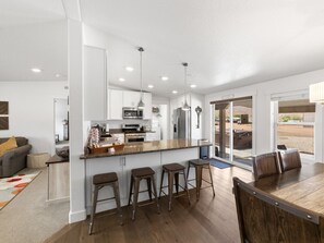 A modern kitchen with a central island, bar stools, and a dining area with a wooden table and chairs.
