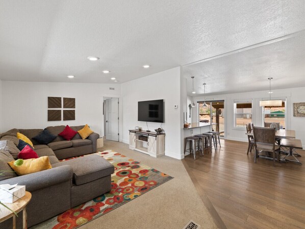 A spacious living room with a grey sofa, colorful rug, and a flat-screen TV.
