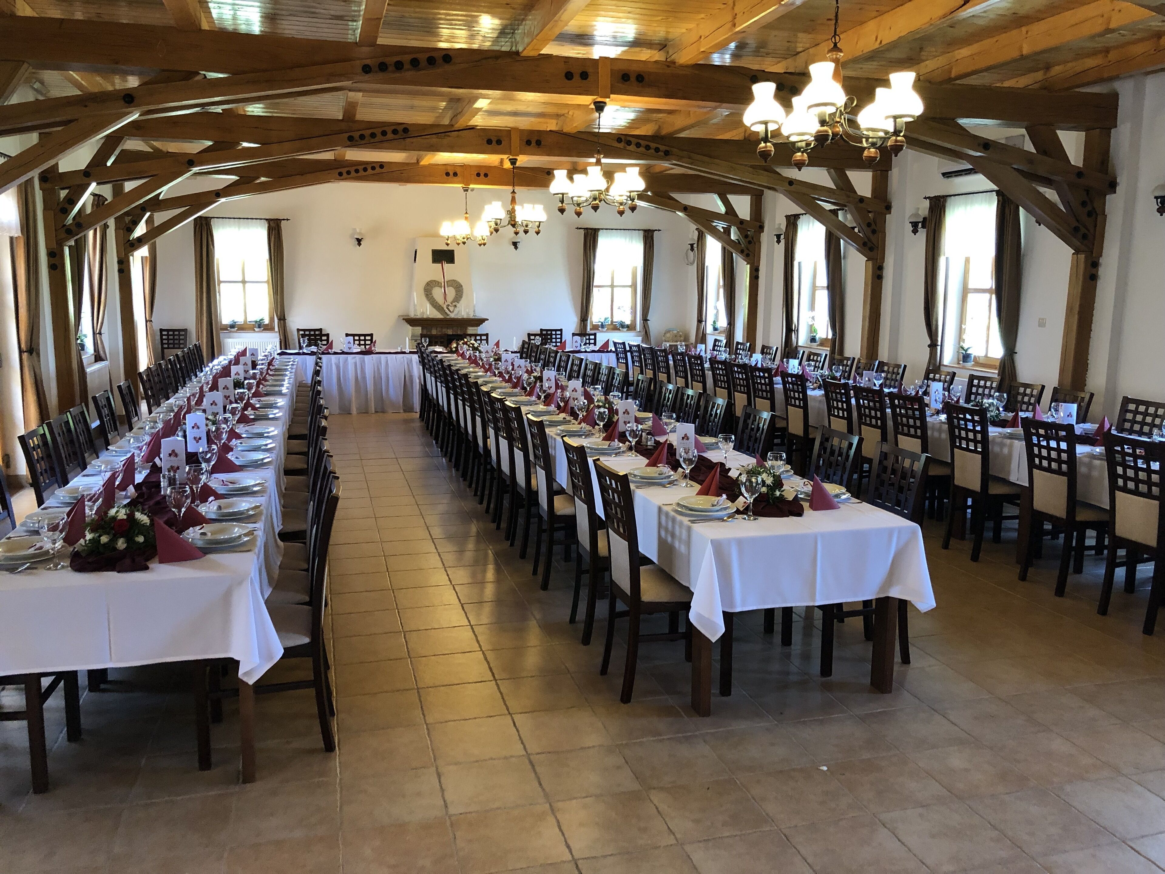 Un amplio salón de banquetes con largas mesas dispuestas para un evento formal, vigas de madera en el techo y candelabros.