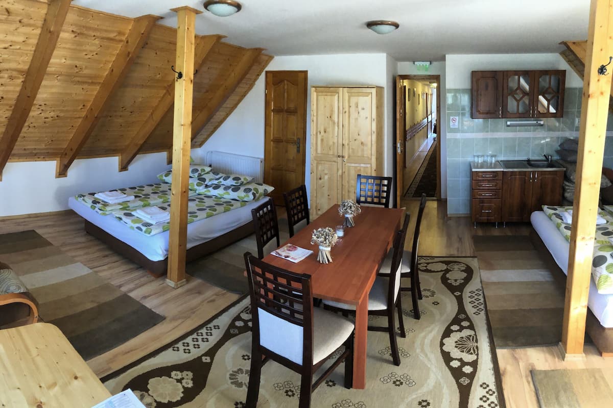 A cozy room with a loft bed, wooden dining table, and a kitchen area.