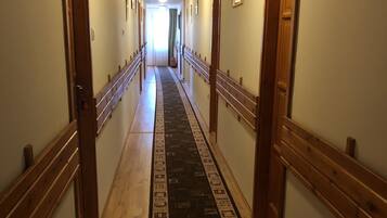 A long hallway with wooden doors on either side, a patterned carpet, and a light source at the end.