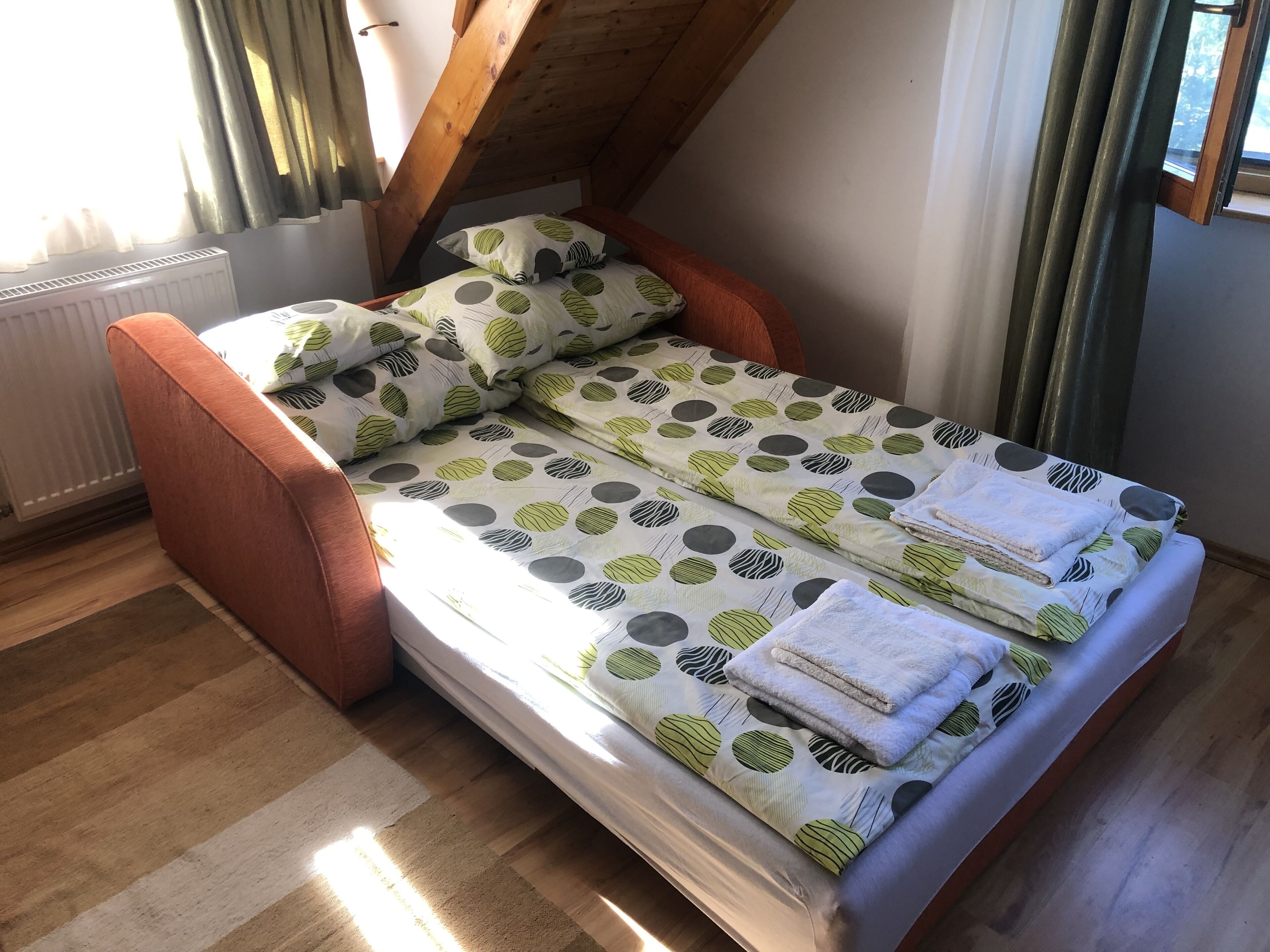 Une chambre de style « loft », avec un plafond en bois, un lit recouvert d’une couette à motifs de feuilles et un radiateur.