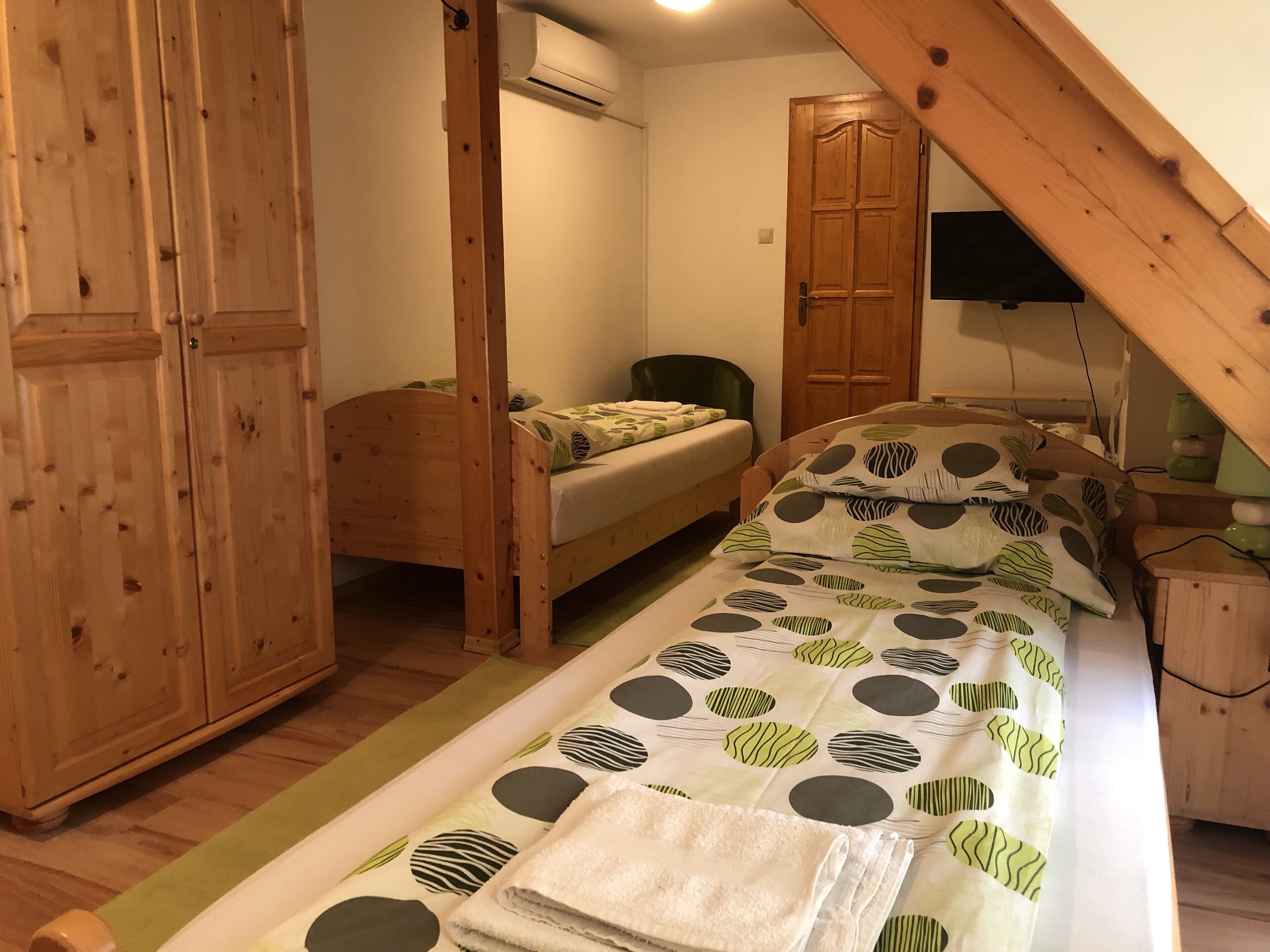 Een slaapkamer met een bed, een houten garderobe, een groene stoel en een houten deur.