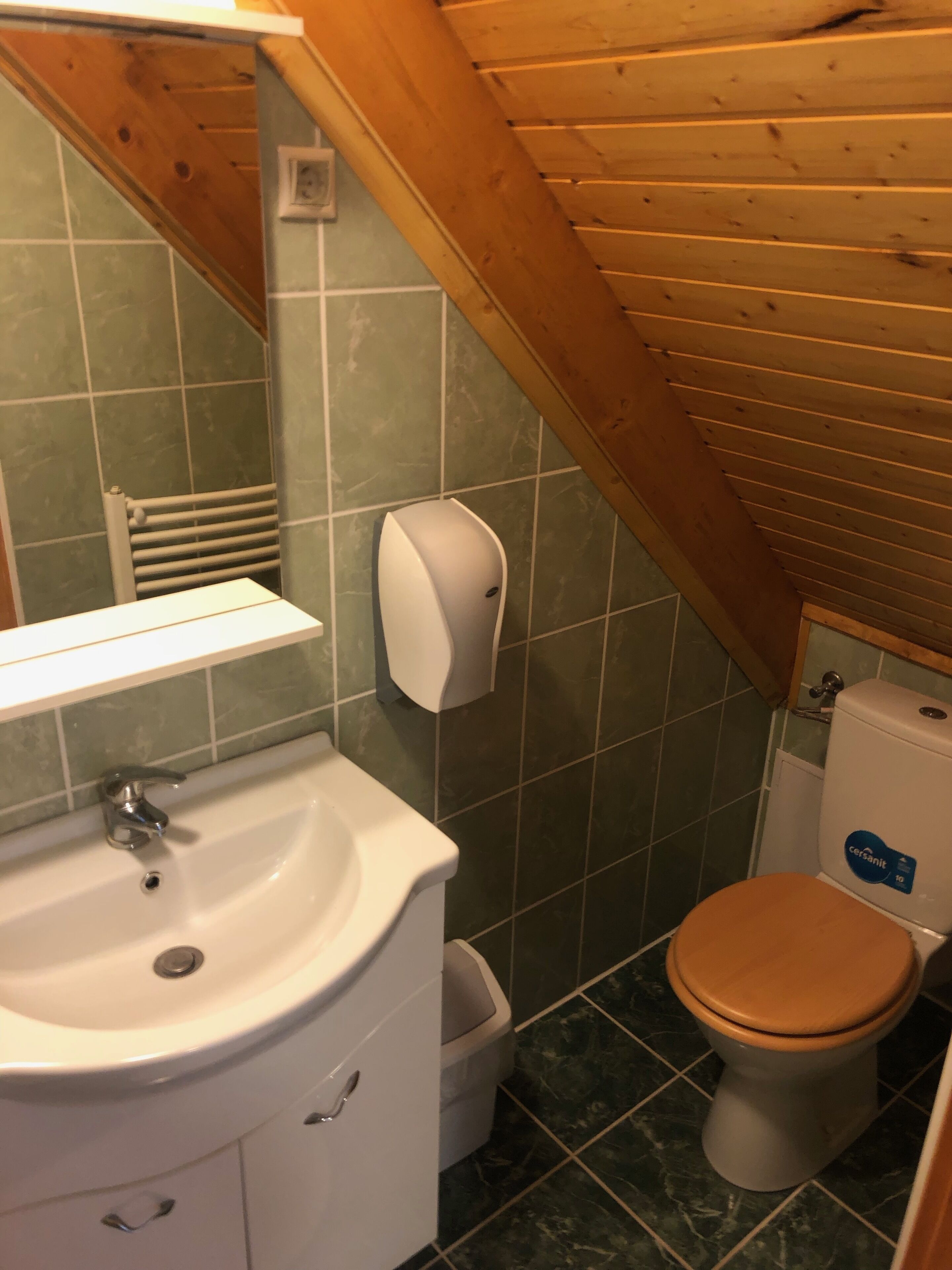 A bathroom with a wooden ceiling, a white sink, a toilet, and a hand dryer.