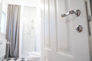 Puerta blanca con pomo y cerradura plateados, que da paso a un baño con ducha y retrete.