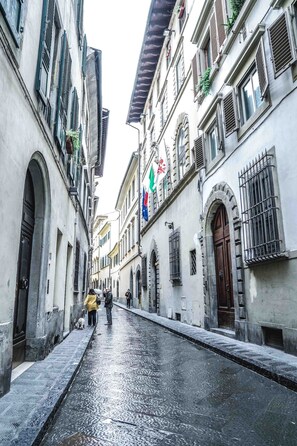 Una calle estrecha con edificios históricos, pavimento mojado y algunos peatones.