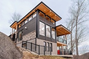 Una casa moderna de varios pisos con fachada de piedra, ventanas grandes y terraza de madera.