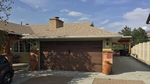 A residential garage with a brick chimney, a covered driveway, and a vehicle parked inside.