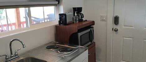 Una cocina compacta con pileta, estufa, microondas y cafetera sobre una encimera de madera.