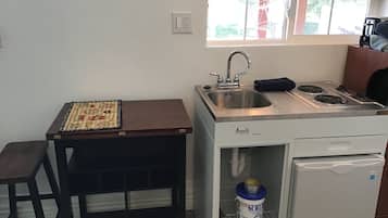 A compact kitchen with a sink, stove, and refrigerator. A small table with a placemat is beside the sink.