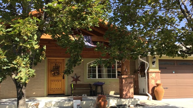 A house with a wooden front door, a bench, a large vase, and a garage door.