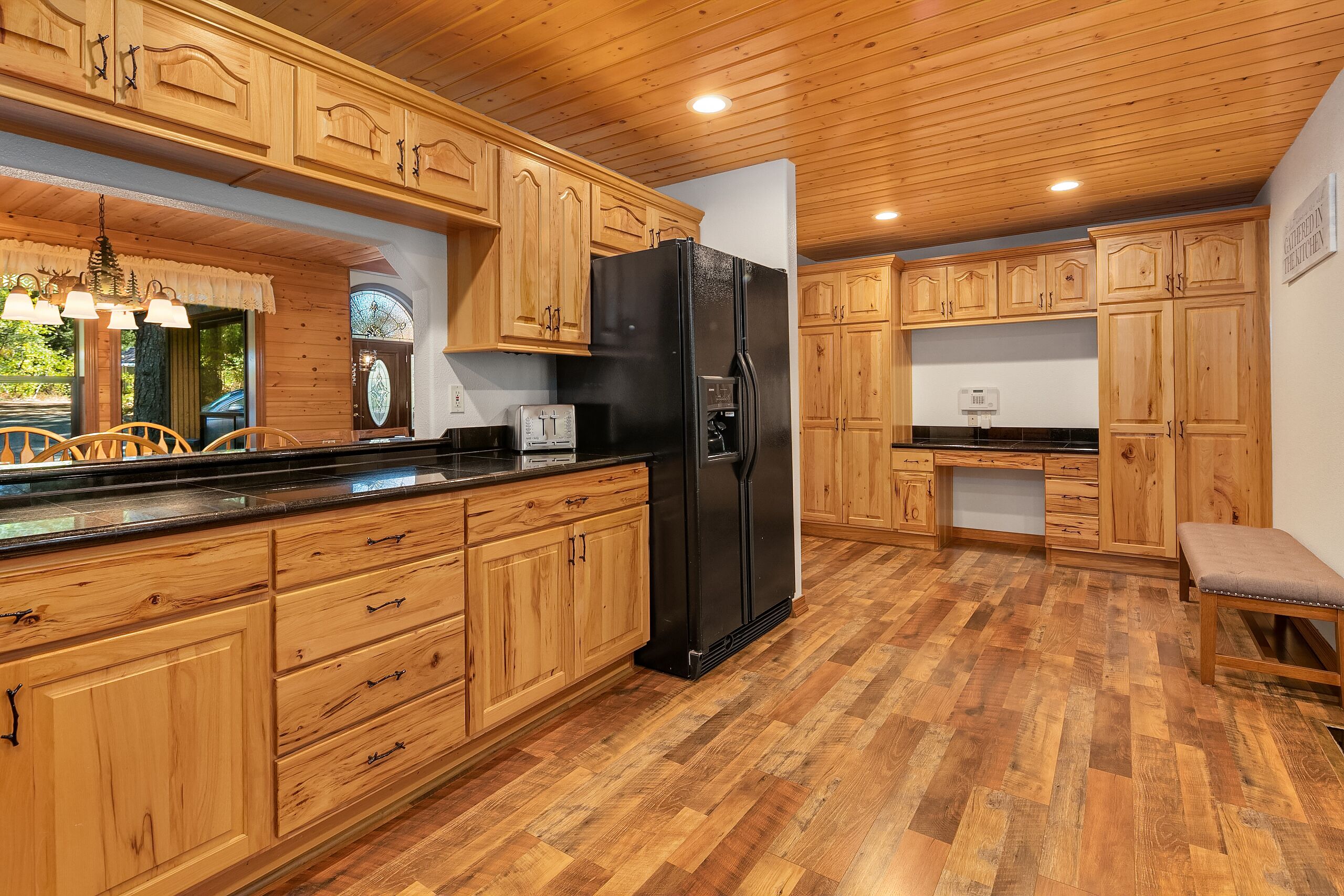 A kitchen with wooden cabinets, a black refrigerator, and a wooden bench.