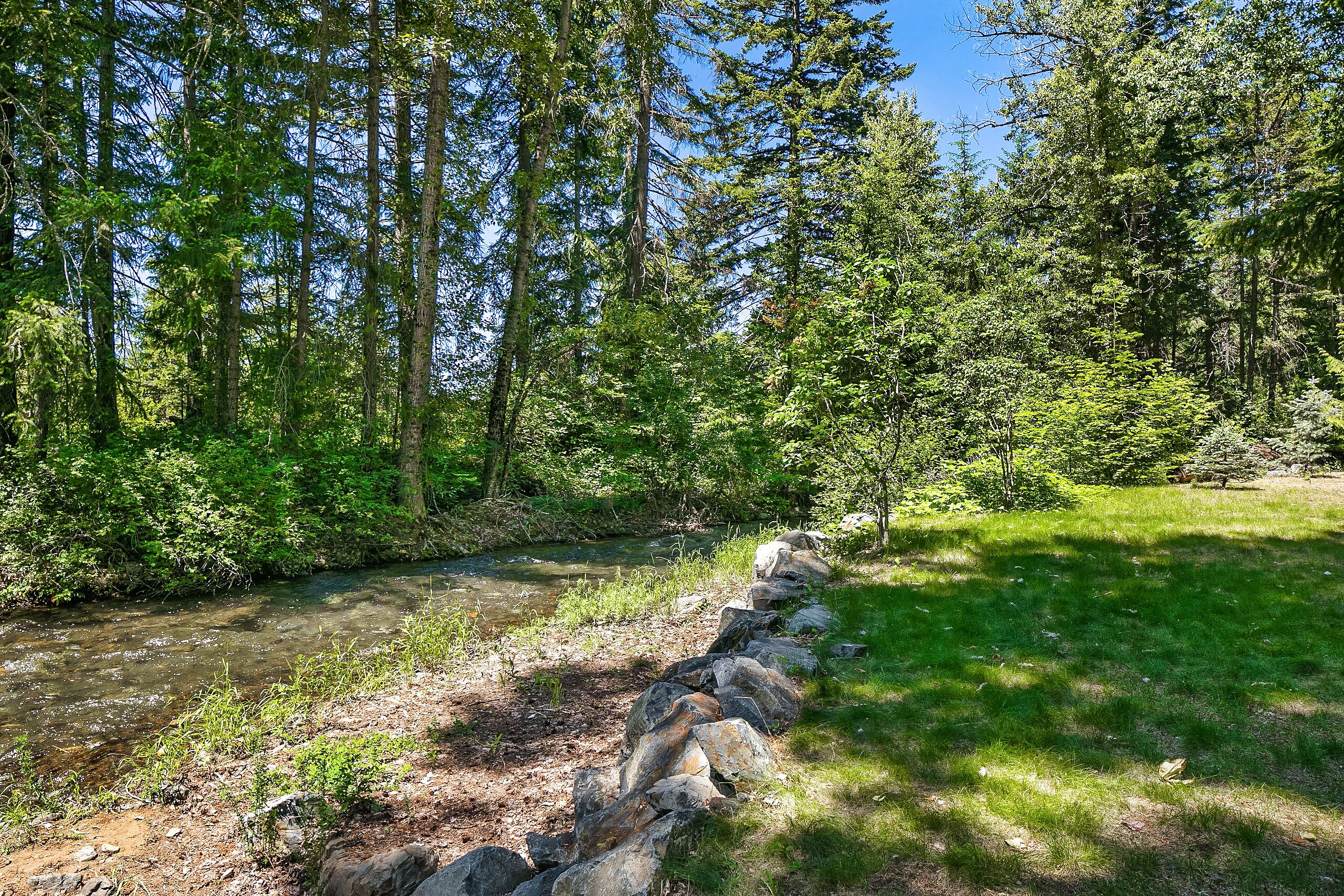 A natural landscape with a river, dense forest, and a stone wall.