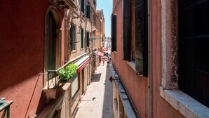 A narrow alleyway with buildings on either side, featuring balconies with plants and a clear sky above. - The Arsenal Large Apartment (Venice)
