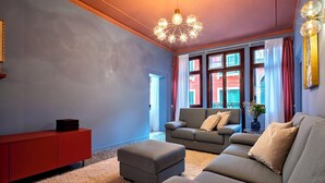A living room with a red cabinet, grey sofas, a chandelier, and large windows with curtains. - The Arsenal Large Apartment (Venice)