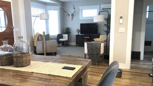 Un salon spacieux avec une table à manger en bois, des sièges confortables, un téléviseur et une décoration murale en forme de bois de cerf.