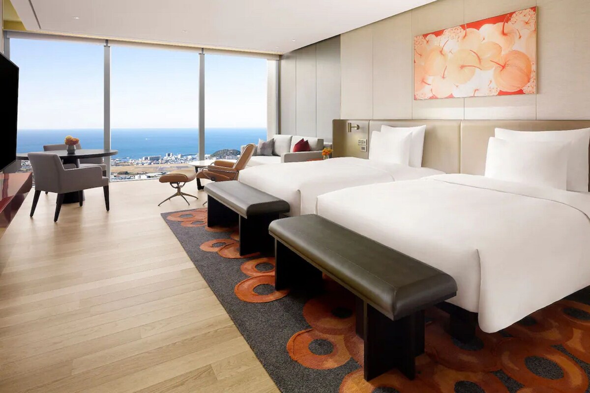 A hotel room with two beds, a desk, a chair, and a view of the ocean.