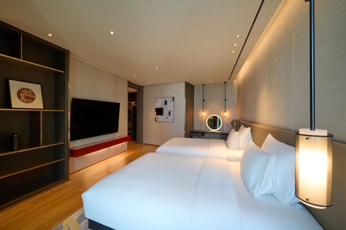 A modern hotel room with a large bed, a TV, a bookshelf, and a bedside table.