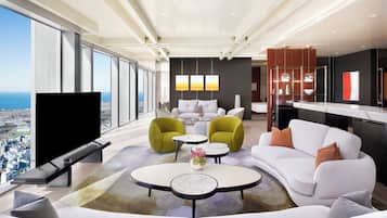 Ein modernes Wohnzimmer mit großem Fernseher, weißen Sofas, grünen Sesseln und einem Essbereich mit einem Glastisch.