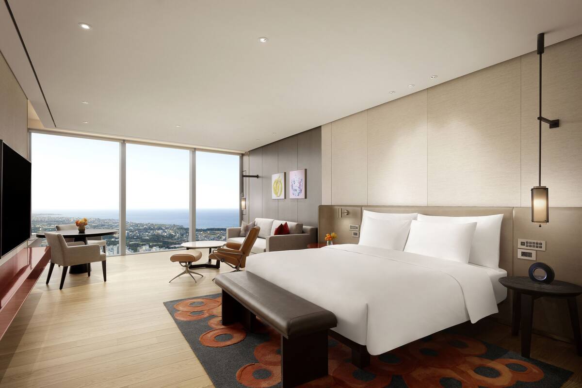 Ein modernes Hotelzimmer mit einem großen Bett, einer Sitzecke mit Blick und einem Esstisch.