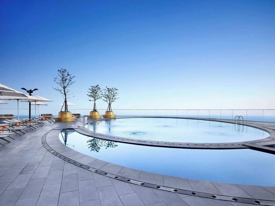 Ein Poolbereich mit Liegestühlen und Tischen, ein klarer Himmel und Blick aufs Meer.