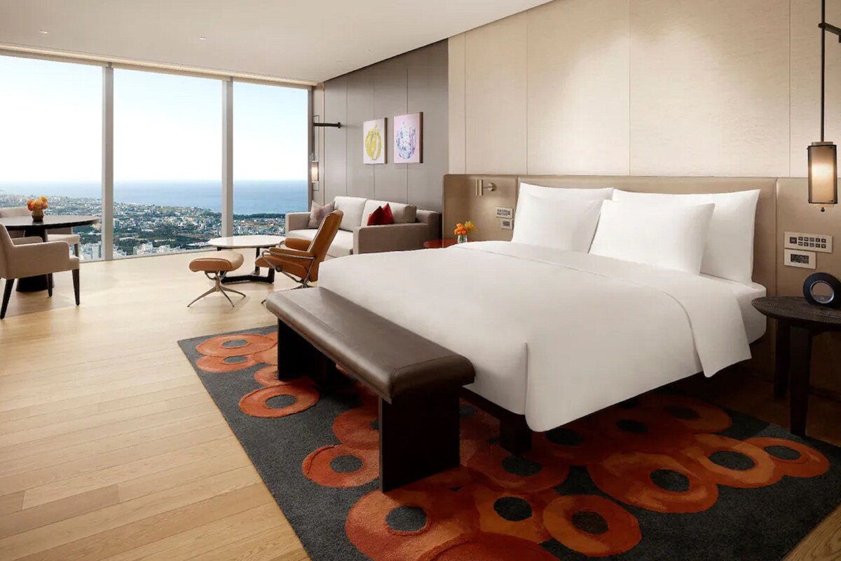 A modern hotel room with a large bed, a desk, and a view of the city.
