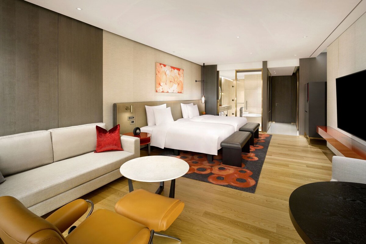 A modern hotel room with a large bed, a sofa, a coffee table, and a TV.