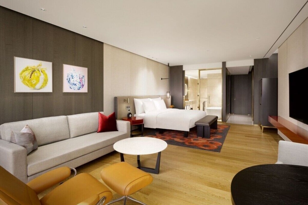 A modern hotel room with a sofa, a bed, a small round table, and a TV.