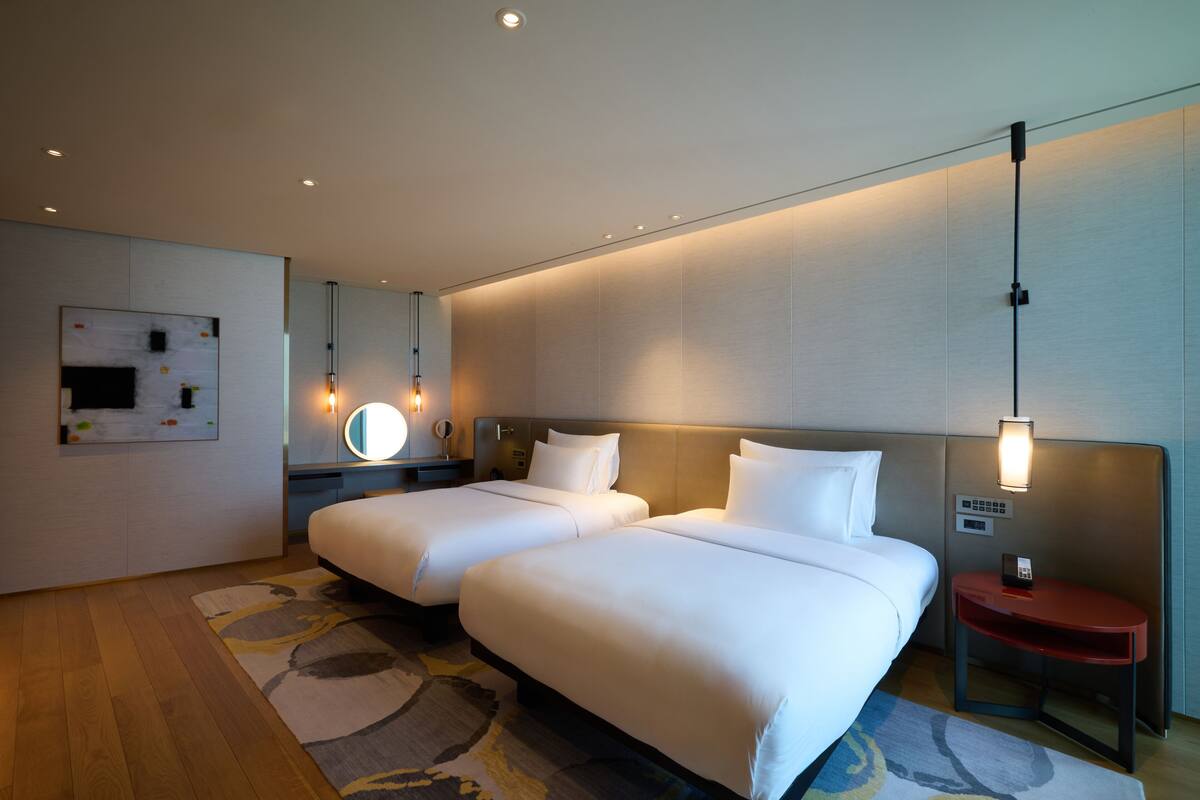 Ein modernes Hotelzimmer mit zwei Betten, einem Nachttisch mit Telefon, einem Spiegel und einer Wandleuchte.