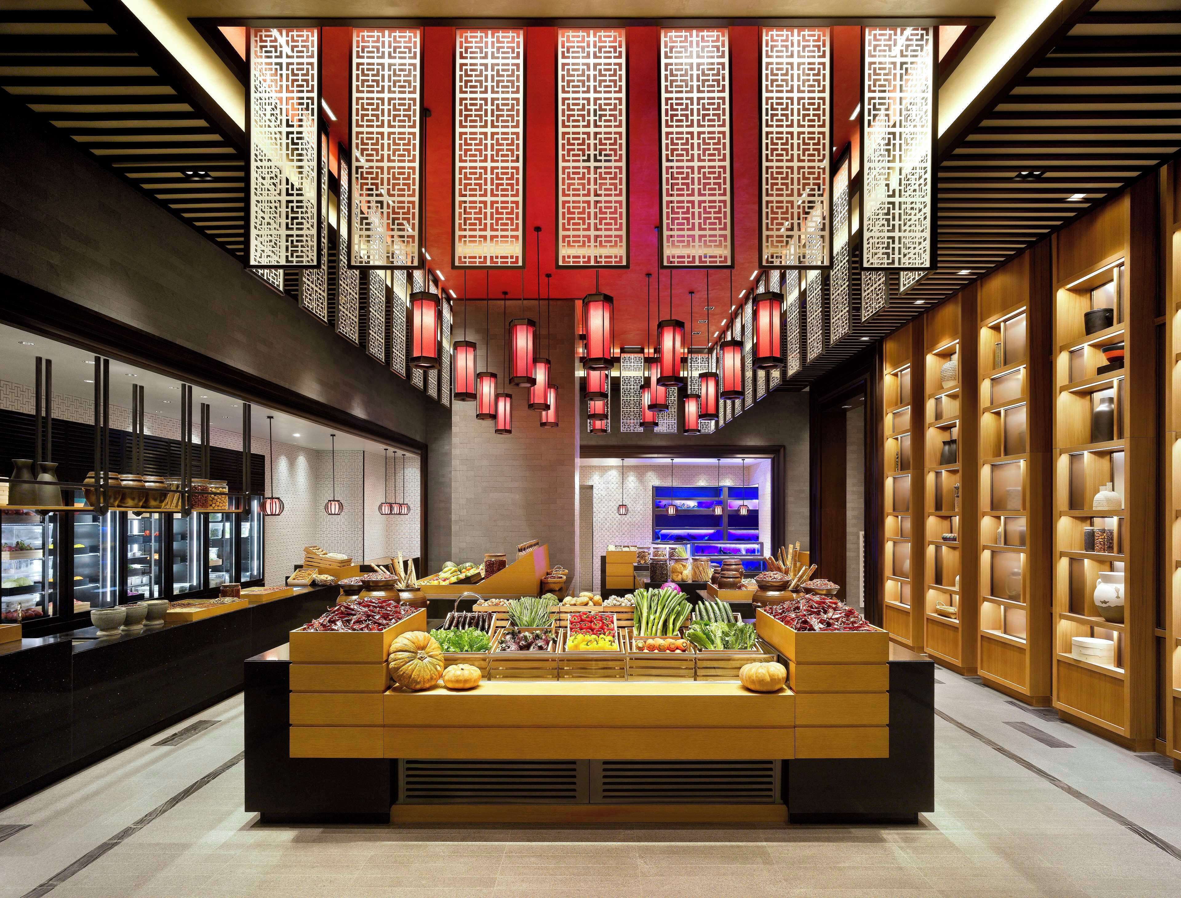 A modern interior with a central display of fresh produce, decorative lanterns, and traditional wall panels.